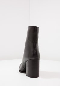 Černá kožená kotníková bota s zaoblenou špičkou, cylindrickým podpatkem a hladkým povrchem. Minimalistický design bez viditelného kovového kování nebo vzorů.