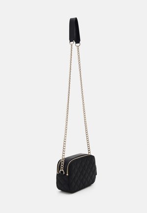 Zwarte, gestikte, rechthoekige crossbodytas met gouden kettingband en bovenzijde ritssluiting op een effen lichte achtergrond.