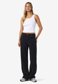Crne traperice širokih nogavica izrađene od trapera s izbljeđenim izgledom, uparene s uskom bijelom rebrastom majicom bez rukava. Model prikazuje ležerni dizajn.