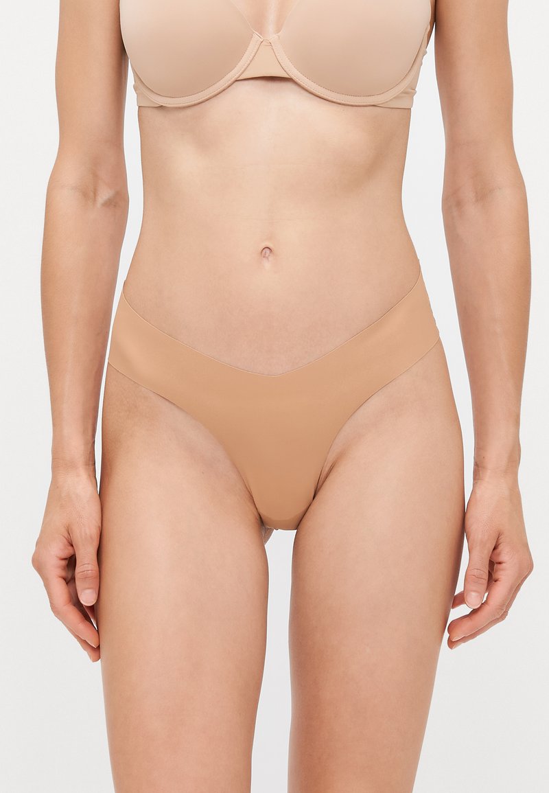 Nude nahtloser Tanga, glatte Textur, niedrig geschnittenes Design mit einem V-förmigen Bündchen. Minimale Abdeckung, minimalistischer Stil und keine sichtbaren Unterwäschelinien.