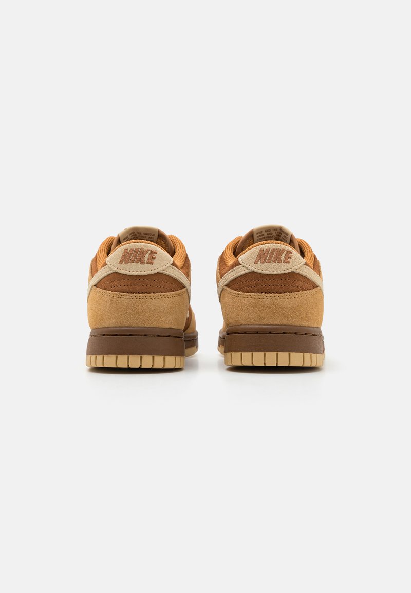 Bruine suède lage sneakers met een gewatteerde kraag, beige en donkerbruine accenten, voorzien van een gestructureerde outsole en "Nike" branding op de hiel.