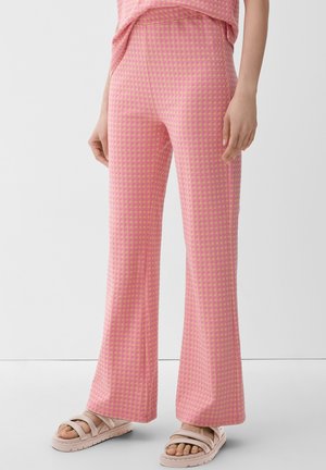Pantalons évasés à carreaux roses et jaunes en tissu texturé, assortis à des sandales plates de couleur claire, avec une taille basse.