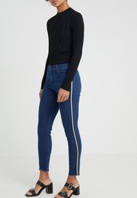 Black ribbed long-sleeve top paired with blue skinny jeans featuring side stripes and distressed hem, complemented by black heeled sandals.