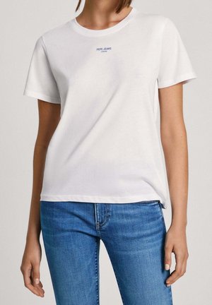 Kobieta ubrana w prosty biały t-shirt z krótkim rękawem z małym logo „PEPE JEANS LONDON”, w połączeniu z niebieskimi dżinsami.