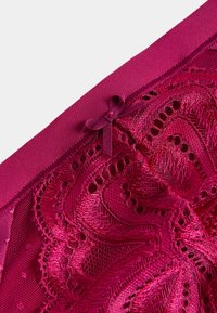 Spetsunderkläder i rik magenta med intrikata blommönster. Har mjukt tyg, satinkant och en central rosett detalj vid midjan.