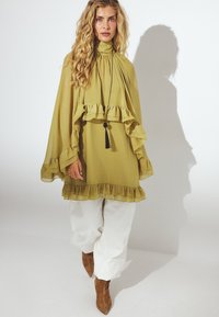 Olīvu zaļa blūze ar volānu piedurknēm un apakšmalu, apvienota ar baltām biksēm. Iekļauj augstu apkakli un melnu pušķi. Strukturēts audums.