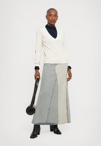 V-neck cream sweater, paired with a color-blocked denim maxi skirt in light and dark shades. Black ankle boots and a round handbag complete the look.
