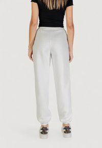 Pantalons de survêtement gris clair en tissu doux, avec une taille élastique et des poignets fuselés. Portés avec des baskets à motifs.