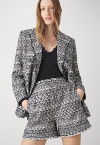 Textured black, white, and blue tweed blazer with double-breasted buttons, paired with matching tweed shorts featuring frayed edges.