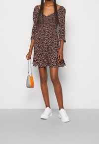 Černé květinové šaty s přiléhavým živůtkem, tříčtvrtečními rukávy a rozšířenou sukní. V kombinaci s bílými teniskami a malou barevně blokovanou taškou.