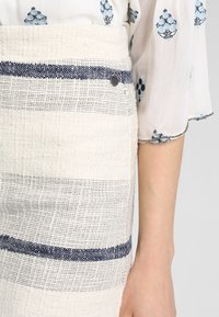 Tessuto bianco testurizzato con strisce orizzontali blu navy, caratterizzato da un dettaglio con bottone metallico sulla cintura. Parte di un indumento.