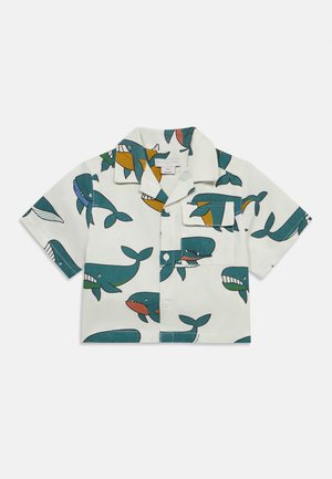 Biała koszula z krótkim rękawem z kolorowymi, zabawnymi ilustracjami wielorybów i kieszenią na piersi z przodu, zapinana na guziki na środku.