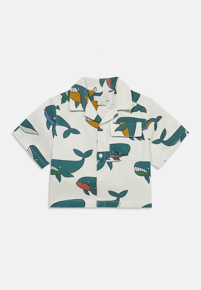 Μπλούζα με κοντά μανίκια σε λευκό χρώμα, διακοσμημένη με πολύχρωμες παιχνιδιάρικες απεικονίσεις φαλαινών και μπροστινή τσέπη στο στήθος, με κουμπιά στη μέση.