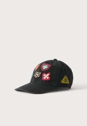 Casquette de baseball noire avec divers patchs brodés colorés, comprenant des blasons, une fleur de lys et un triangle jaune avec un symbole d’arbre.