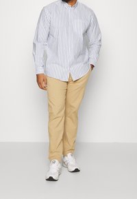 Vaaleansininen ja valkoinen raidallinen nappipaita, jossa on rintatasku, yhdistetty beigen värisiin chinoihin ja valkoisiin tennareihin. Rento malli, pitkät hihat.