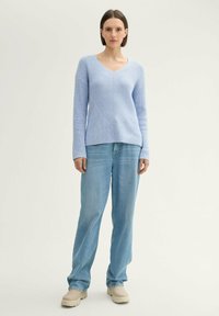 Lichtblauwe ribgebreide trui met een V-hals en diagonaal textuurpatroon, gecombineerd met lichtblauwe rechte jeans en beige schoenen.