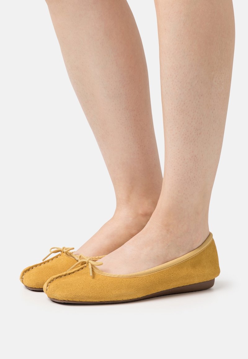 Ballerines en daim jaune avec un bout arrondi, un petit talon et un détail de nœud noué à l'avant. Doublure intérieure lisse et bords cousus.
