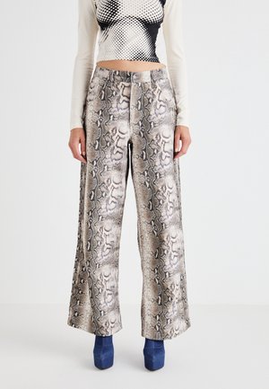 Person iført højtaljede, vidbenede bukser med slangeskindsmønster kombineret med blå platformsko og en langærmet crop top med sort-hvidt mønster.