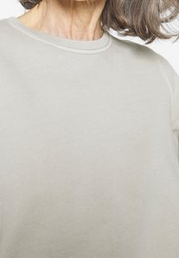 Sudadera de color gris claro, texturizada, con cuello redondo y detalles acanalados, que presenta un ajuste relajado y una tela suave.