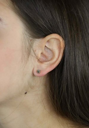 Srebrne kolczyki wkrętki w kształcie róż, z misternymi detalami. Noszone na uchu osoby z ciemnymi włosami, widoczne w zbliżeniu.