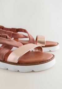 Sandačky s otevřenou špičkou, růžovými semišovými popruhy, kovovými akcenty v odstínu růžového zlata, hnědými koženými stélkami a bílými gumovými podrážkami s texturovaným povrchem.