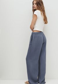En lätt, kortärmad vit t-shirt som kombineras med lösa, texturerade navyblå vida byxor med elastisk midja och sidofickor.