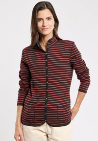 Schwarzes Langarm-Hemd mit roten horizontalen Streifen. Verfügt über einen Stehkragen, zwei Fronttaschen und einen abgerundeten Saum.