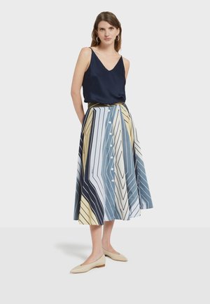 Donna che indossa un top senza maniche blu navy e una gonna midi a vita alta con bottoni frontali e righe geometriche multicolori, abbinata a ballerine beige.