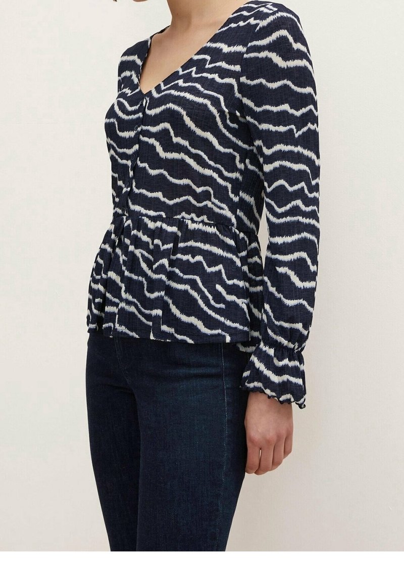 Navy blue peplum top with white zigzag pattern, V-neck, long sleeves with ruffled cuffs, textured fabric, and front button details.