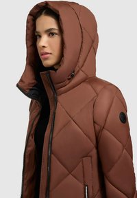 Brūna bieza pūkaina jaka ar kapuci, ar melnu rāvējslēdzēju un sānu kabatu. Gluda tekstūra un dimanta formas šuvju raksts.