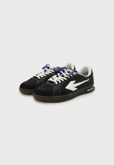 Paire de baskets basses noires avec logo flèche blanc, lacets blancs et violets, et semelles translucides marron avec texte "OFF" sur le côté.