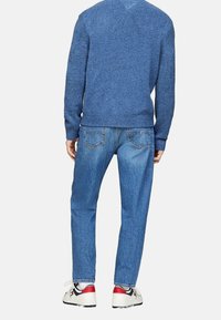 Blå stickad tröja, ljusblå jeans och vita sneakers med röda och svarta accenter. Tröjan har ribbade avslut och ärmar.