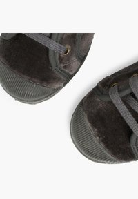 Černé semišové tenisky s gumovými podrážkami, kulatými špičkami a šedými tkaničkami. Obsahují zlaté očky a vroubkované špičky. Texturovaný povrch.