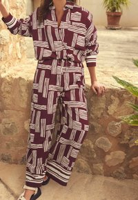 Tenue couleur vin avec motifs à rayures blanches, comprenant une chemise à col et un pantalon ample. Fabriquée en tissu léger, avec une taille élastique.