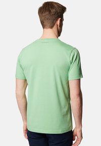 Zielona bawełniana koszulka z klasycznym okrągłym dekoltem, krótkimi rękawami i gładkim tyłem, z małą metką przy kołnierzyku.