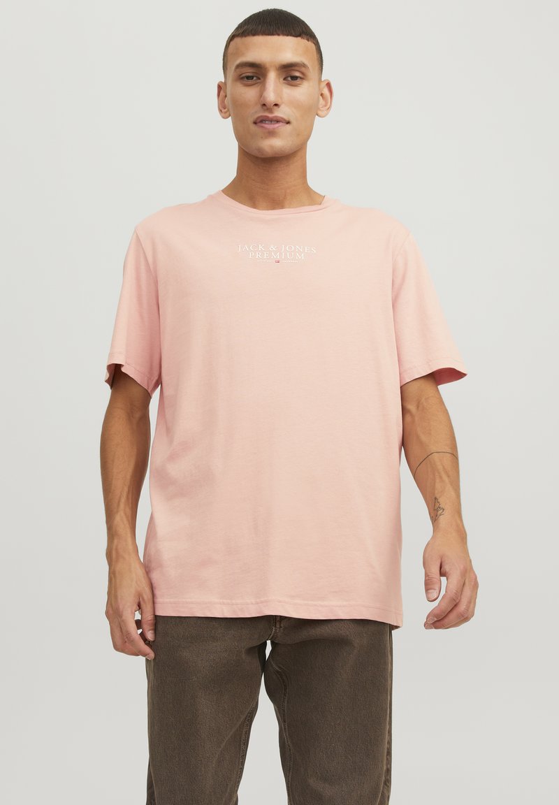 Lichtroze T-shirt met korte mouwen van katoen, met een ronde halslijn en een klein wit logo op de borst. Eenvoudig en casual ontwerp.