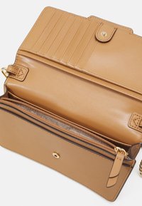 Portefeuille en cuir tan avec plusieurs emplacements pour cartes, compartiment zippé et fermeture à pression. Présente une texture lisse et des accents en matériel doré.