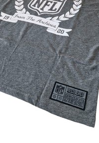 Gray t-shirt made of soft fabric featuring a large white NFL logo, a decorative leaf pattern, and a black label with "RECOVERED" text.