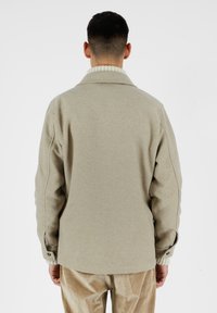 Giacca in misto lana beige con colletto, polsini a coste e dettagli con bottoni, presenta una vestibilità rilassata e una trama liscia.