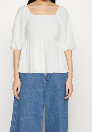Top bianco a peplo con scollatura quadrata, tessuto strutturato e maniche a sbuffo, abbinato a jeans blu a gamba larga.