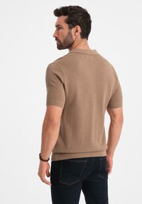 Kortärmad, brun stickad polo med en strukturerad yta. Har ribbad krage och manschetter, kombinerad med mörka jeans.