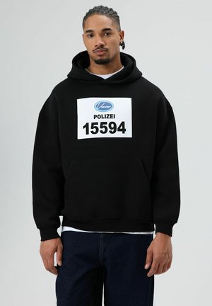 Zwarte hoodie met een grote witte tekst op de voorkant met de tekst "POLIZEI 15594" en een blauw logo. Voorzien van een kangoeroezak en geribbelde manchetten.