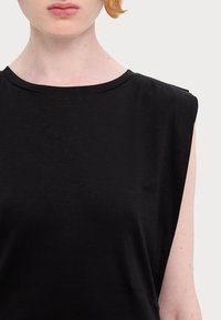 Czarny bezrękawnik z okrągłym dekoltem, miękka faktura i minimalistyczny design. Lekko zaznaczone ramiona dodają subtelnego detalu.
