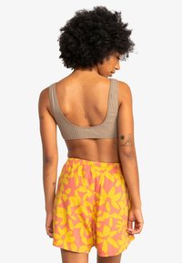 Top corto acanalado beige con tirantes anchos, combinado con pantalones cortos rosas con grandes patrones de flores amarillas y una cinturilla elástica.