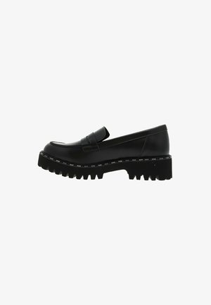 Mocassin en cuir noir avec un bout arrondi et une semelle épaisse et texturée. Il présente un dessus lisse et une sangle décorative sur le cou-de-pied.