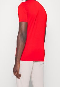 Camiseta de manga corta roja hecha de tela suave con cuello redondo. Presenta sutiles detalles de costura y una silueta ajustada.