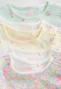 Cinq bodies pour bébé en couleurs pastel avec motifs floraux, texture côtelée et fermetures à pressions aux épaules, disposés à plat en couches.