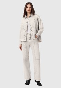 Lichtgrijs denim jack en bijpassende broek met een losse pasvorm, voorzien van stikseldetails en zijzakken. Gecombineerd met zwarte laarzen met hoge hak.