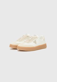 White canvas sneakers with beige suede accents, round toe, flat gum rubber sole, and embossed logo detail on the tongue and side.