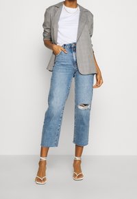 Grå rutigt blazer, vit t-shirt och slitna ljusblå cropped jeans. Vita sandaler med remmar kompletterar outfiten.